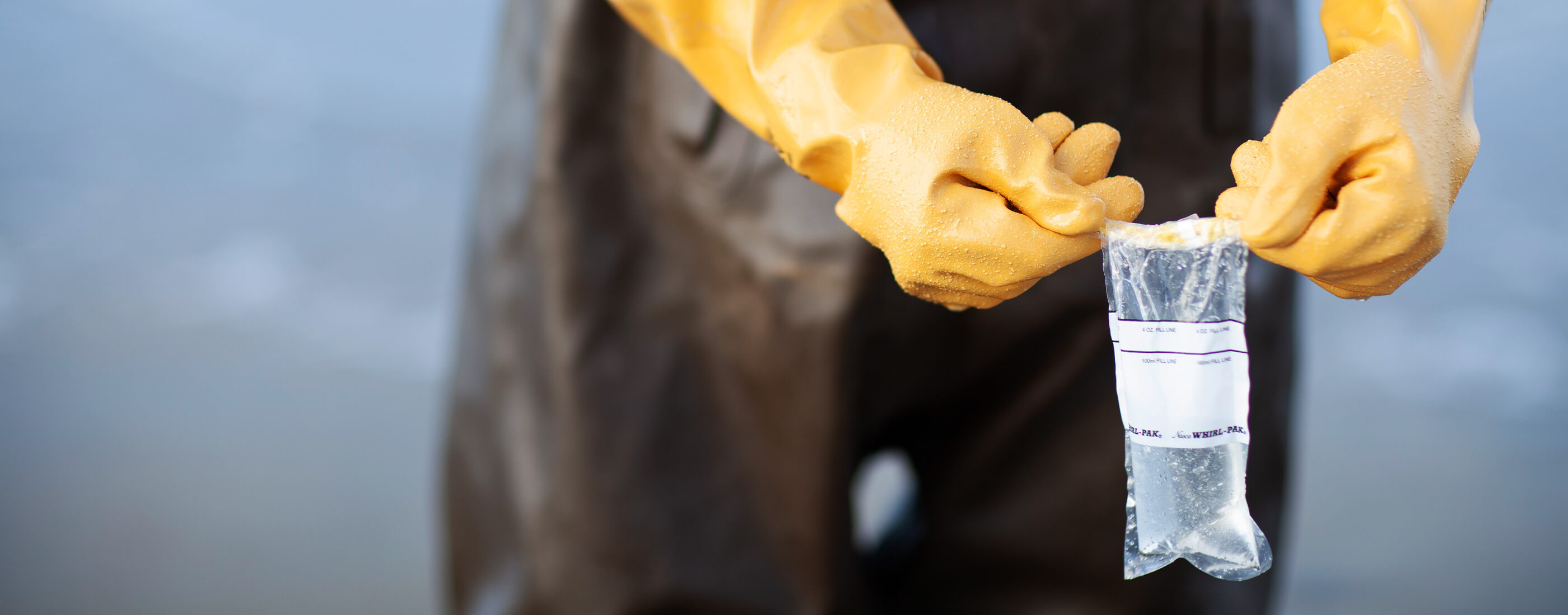 Hands in yellow gloves hold up a water sample